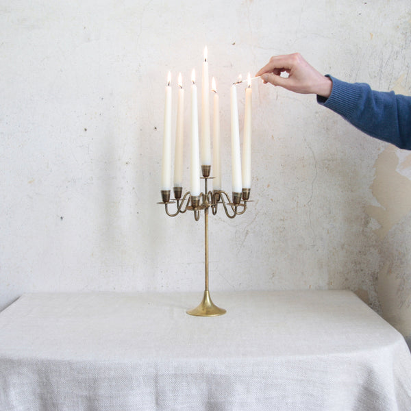 Person lighting candles on an elegant Swedish seven-headed brass candelabra, 1950s. A striking mid-century Nordic design combining classical form with modern simplicity.