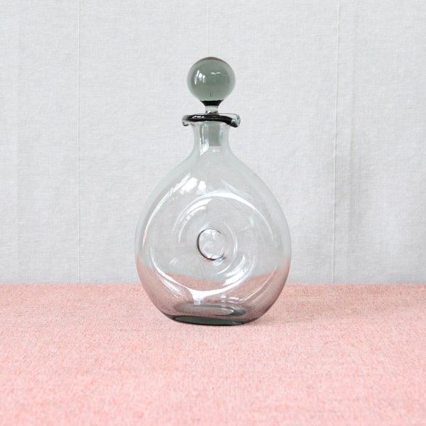 A 1953 Per Lütken ‘Danica’ decanter, or “donut / doughnut decanter” with circular body and solid ball shaped stopper. The sophisticated greenish-grey colour of the glass is known as 'Smoke', and was Lütken's signature colour way at Holmegaard.