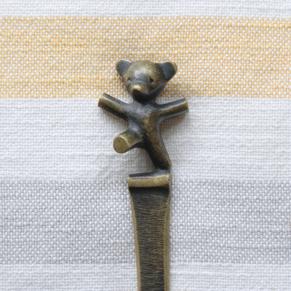 Bronze teddy bear figurine on a striped fabric background. Mid-century Walter Bosse brass bear cub letter opener, produced by Herta Baller in Vienna. Available from Art & Utility, specialists in Modernist Austrian brass.