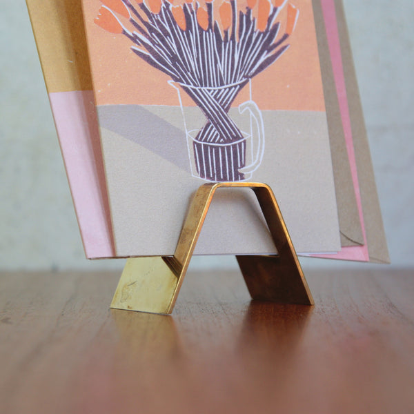 Vintage Hagenauer brass letter rack or card stand, stamped with all of Werkstätte Hagenauer's marks. The shiny gold stand holds a card with a floral design.