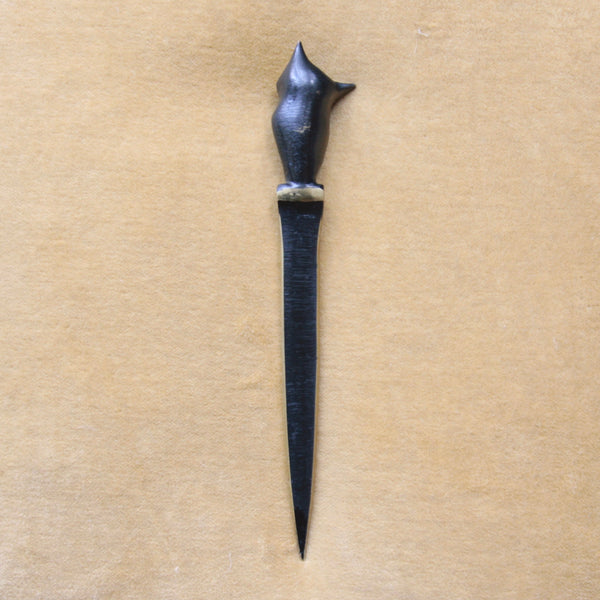 Black patinated letter opener with a unique handle design that incorporates a stylised Modernist owl. The background is a golden yellow.