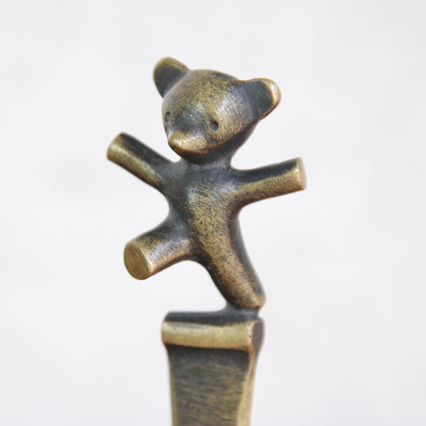 Close up of a bronze teddy bear figurine on a white background. Vintage Walter Bosse brass letter opener with bear cub figure, produced by Herta Baller. UK design gallery Art & Utility offer worldwide shipping.