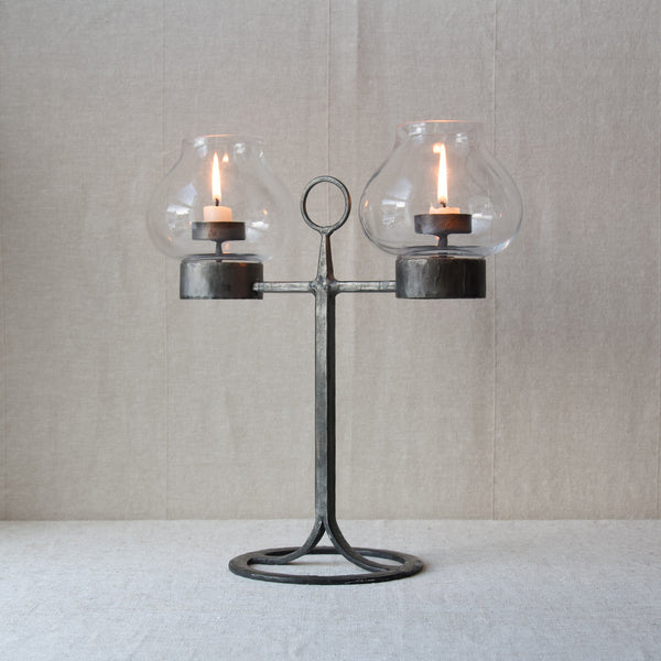 A lit candelabrum by Bertil Vallien for Boda Smide. This candlestick holder is intended to be used with tea light candles and can be carried from room to room by the circular loop in the centre.