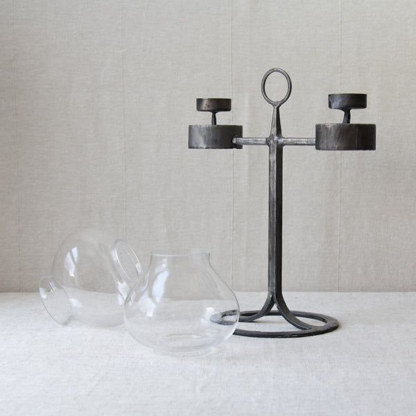 A deconstructed candelabrum by Bertil Vallien. The candelabra's glass hurricane lampshades stand to the left of the hand-forged black iron candelabrum.