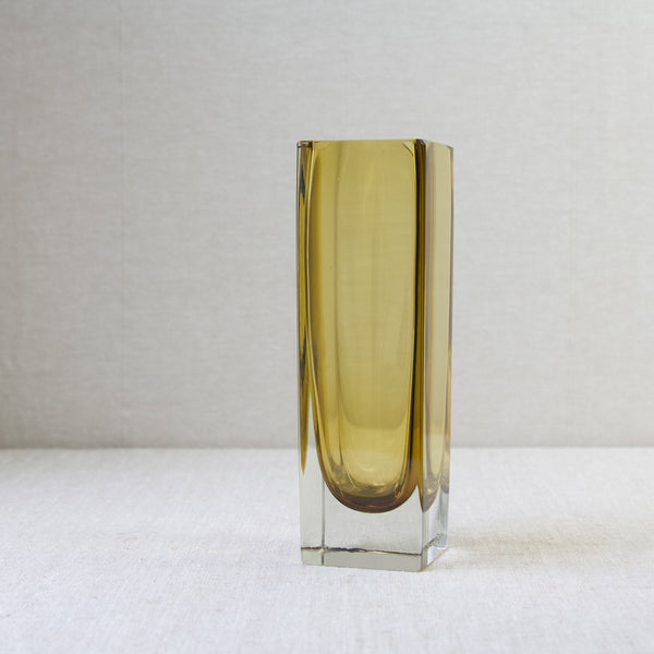 Mood image showing a tall rectilinear square shaped vase in yellow coloured glass. This design is model 296 designed by Kaj Franck in 1964 for Nuutajärvi Notsjö, Finland.