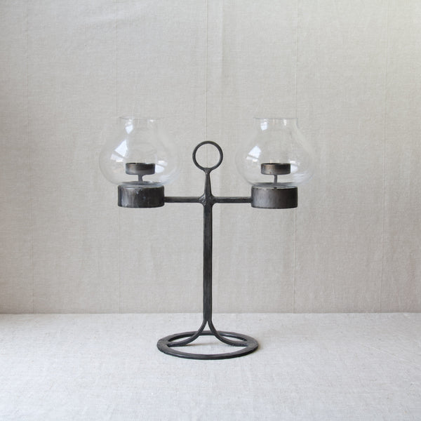 Far away shot of a Bertil Vallien candelabrum or candelabra made by the expert metalworks of Boda Smide. The two clear glass hurricane lampshade were handblown at Kosta Boda glassworks.