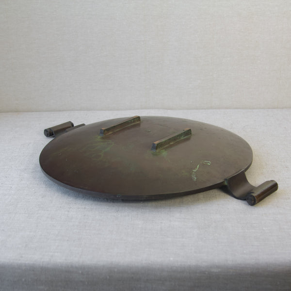 Top down view of the underside of a large circular dish with two handles. The tray is solid cast bronze and was produced by Swedish brothers Einar & Sune Bäckström in the 1930s.