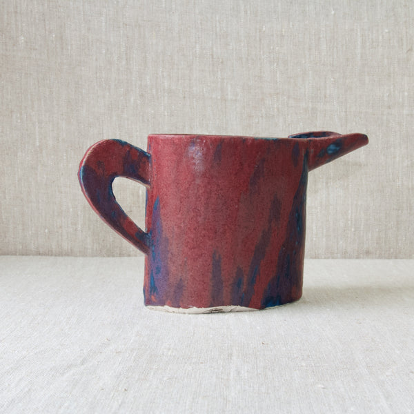 Reverse view of an Emmanuel Cooper jug with a velvety purple, pink, red, and blue glaze. This is a very tactile piece of British Studio Pottery.. 