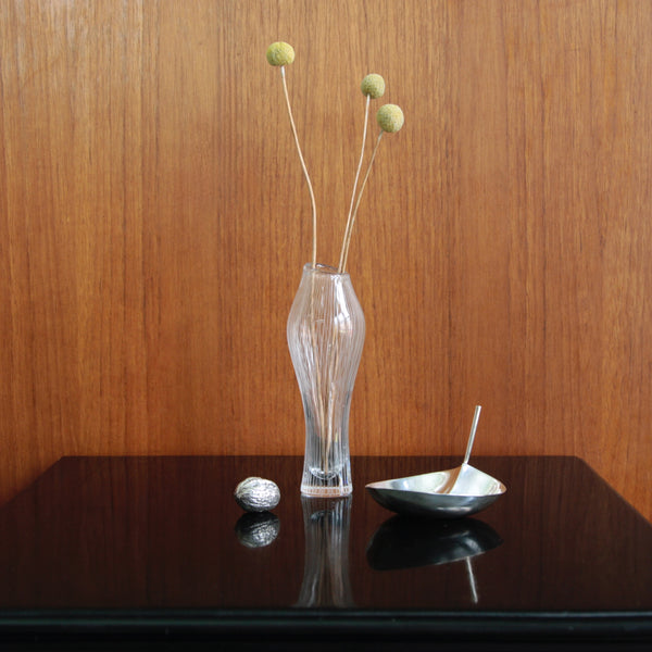 Still life mood shot featuring Modernist designes by Tapio Wirkkala, including a Varsanjalka bud vase in clear glass, and a model TW1 sterling silver leaf-shaped bowl. Both design exhibit a sculptural organic form, and they are signed examples.