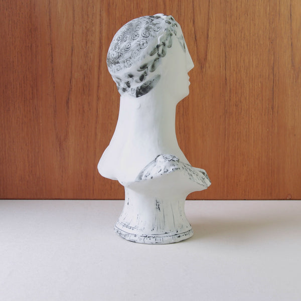 Vintage Modernist white porcelain sculpture by Susan Parkinson, inspired by ancient Greek portraiture and mid-century British design. Item is on a linen tablecloth and in front of a wooden backdrop. 