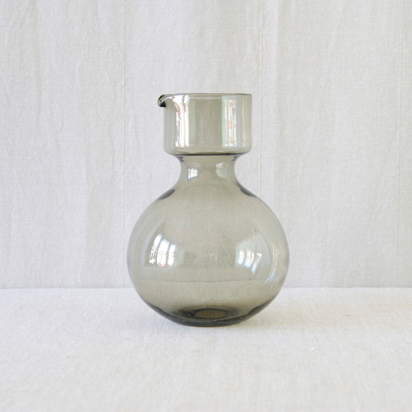 Smoke-grey round glass pitcher with a wide bulbous base and a short cylindrical neck, forming the broad lower section of Kaj Franck's Kremlin Kellot stacking juice set.