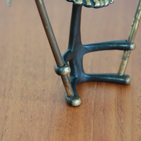 Detail of finish on a mettalic mid-century gnome ornament by Walter Bosse, holding miniature gardening tools.