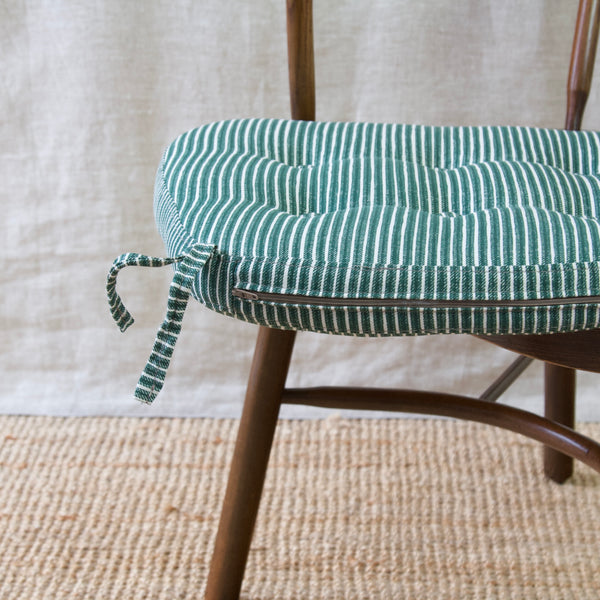 Close up of a Fermoie upholstered cushion. The striped fabric is green and white. The cushion belongs to a vintage Niels Eilersen Scandinavian Windsor chair, boasting steam-bent wood in a dark walnut colour.