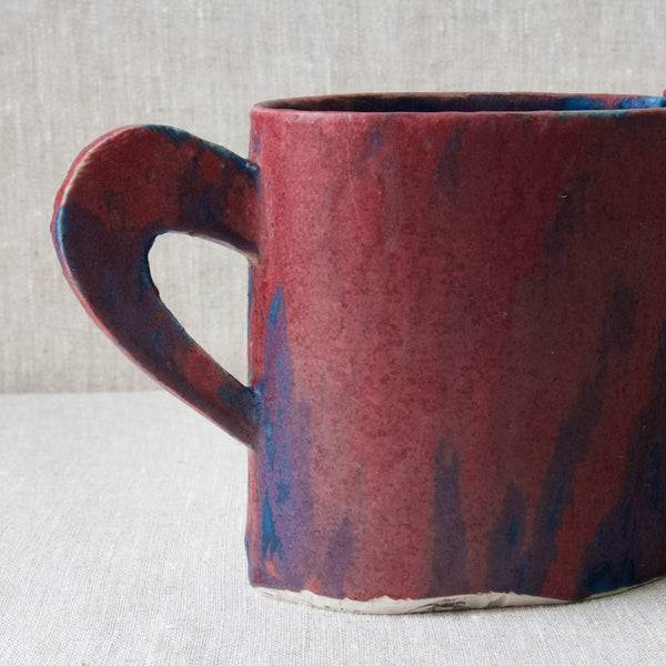 View of the back of an Emmanuel Cooper jug where the slab cut handle is joined. The colourful glaze has shapes in it similar to flames or stripes.