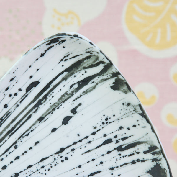 A close-up of a white ceramic plate with black paint splatter and brushstroke patterns. Design by Susan Parkinson for The Richard Parkinson Pottery, in Brabourne Lees, Kent