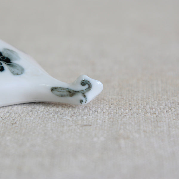 Close-up of a white ceramic tail belonging to a Loch Ness Monster figurine. The tail fin is hand-painted with a scroll motif. Created by Susan Parkinson this Nessie ornament is an exceptionally scarce Richard Parkinson Pottery design whose commercial production remains uncertain.