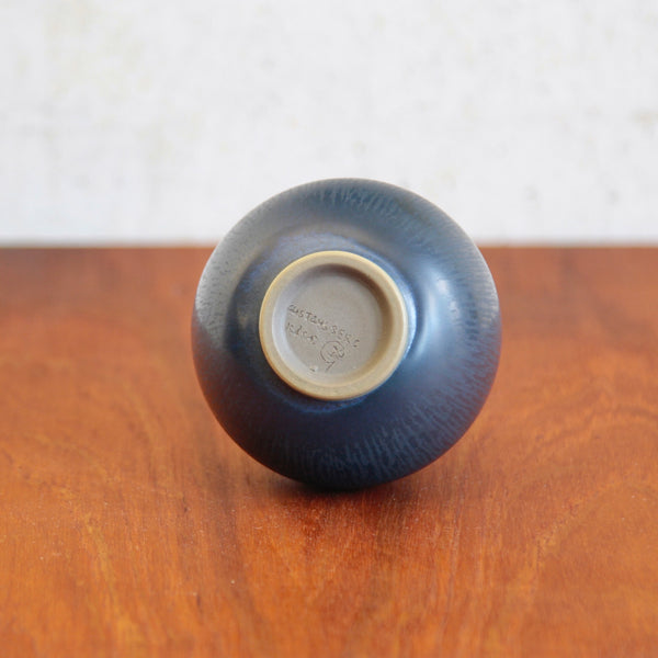 Underside or base of a Wilhelm Kage vase. The Swedish ceramic vase is hand inscribed with the Gustavsberg monogram design of a capital G with an anchor. The bottle is also signed with Kåge's name and the date letter V for 1952.