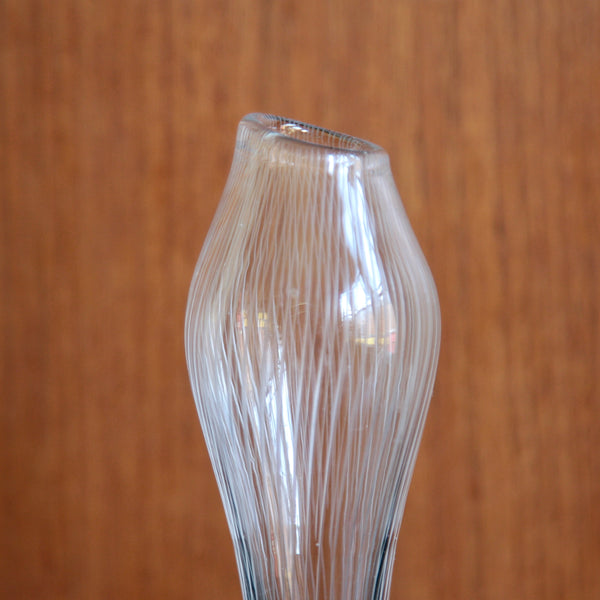 Clear glass vase with ribbed design against a wooden background. The lines are hand-cut and the vase is hand-blown. Tapio Wirkkala Varsanjalka vase, elegant biomorphic shape, 16cm, offered by Art & Utility in the UK.