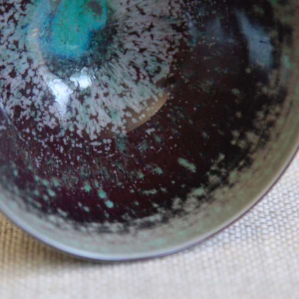 Close-up of a ceramic bowl with a textured surface on a fabric background. Swedish modern porcelain bowl by Friberg featuring amethyst tonal bands; highly collectable Gustavsberg studio ceramic art.