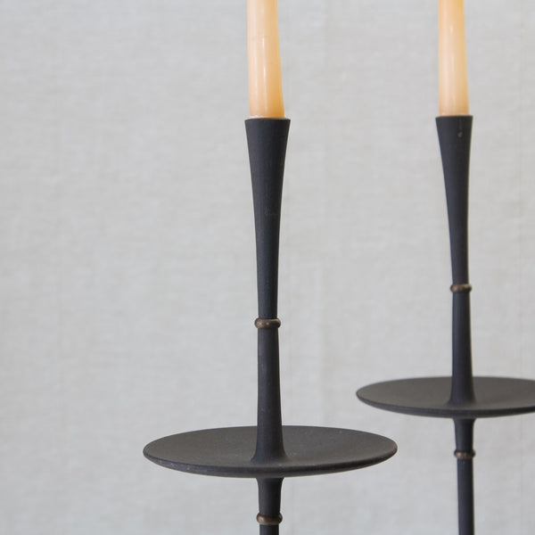 Detail of the slender elongated form of a MidCentury Modern candlestick in black cast iron. The slender sculptural parts of the candlesticks are separated by little brass disks. This design we call "Satellite" is by Jens Quistgaard. 