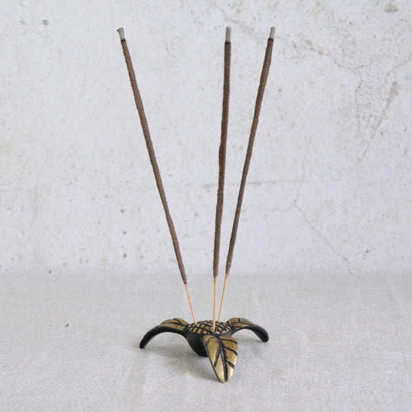 Incense stick holder with three incense sticks on a textured white background. Collectible Walter Bosse floral incense holder by Herta Baller, Vienna. Available from UK gallery Art & Utility, experts in Austrian brass.