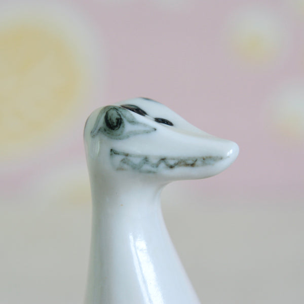 A close-up of a glossy white ceramic Loch Ness Monster figurine with hand-painted black facial details. 1950s British Modernist ceramic design by Susan Parkinson. Nessie with streamlined sculptural form and expressive decoration is both a rare and beautiful design.