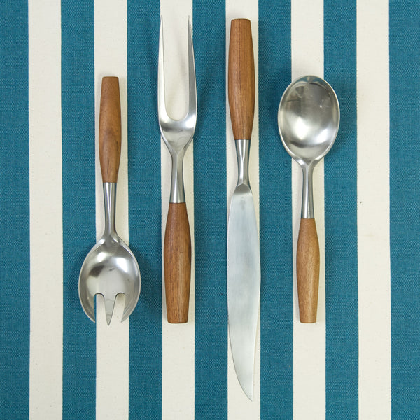 Four pieces of serving flatware, left to right; a serving fork, carving fork, carving knife, and serving spoon. All pieces were designed by Jens Quistgaard for Dansk Designs.