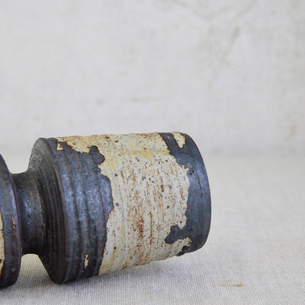 Cylindrical ceramic object with a textured surface on a light fabric background. Annikki Hovisaari Graphic Glaze Hourglass Vase Mid-Century-Modern Nordic.