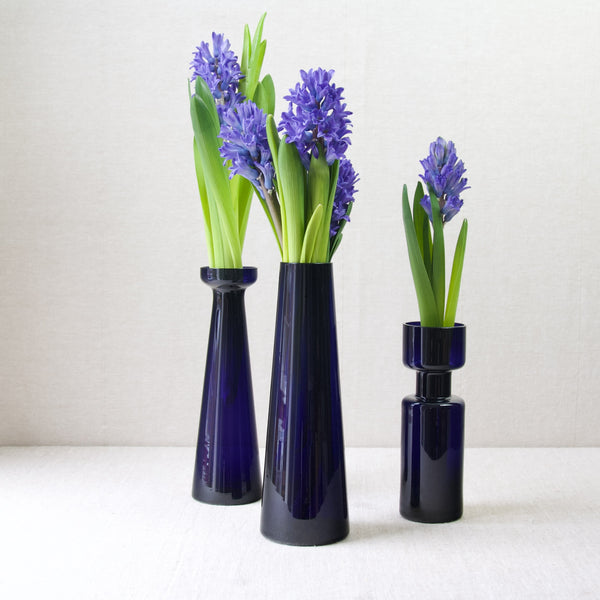 Three geometric Nuutajarvi Notsjo Finnish glass vases designed by Kaj Franck and Saara Hopea, demonstrating the clean and minimalist aesthetic of Finnish Modernism. The vases have blue hyacinth flowers.