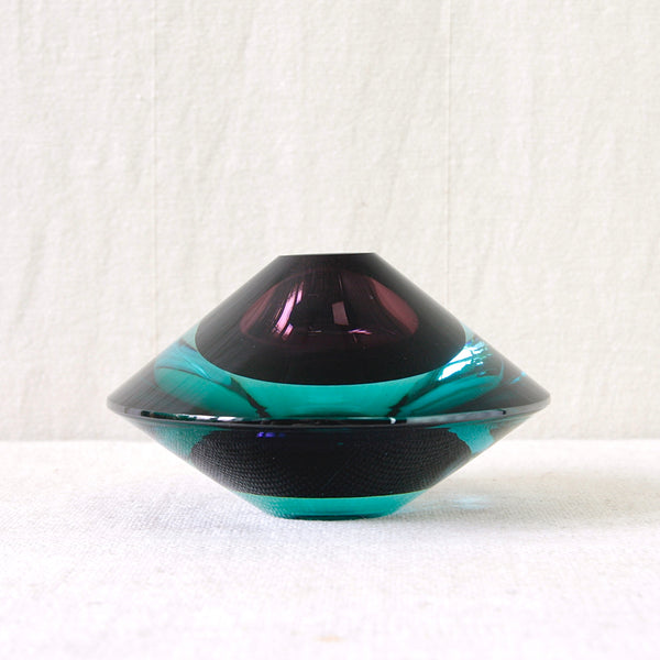 Side view of Kaj Franck's 1956 KF 235 Flying Saucer, showing the broad geometric profile, dark purple and electric blue Finnish art glass appearing to hover above the surface.