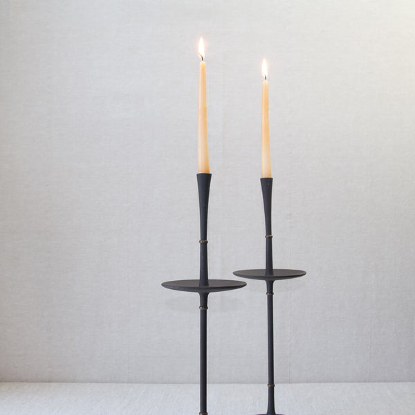 Head on shot of the top half of a pair of Jens Quistgaard cast iron candlesticks. The candle holders are made from black cast iron metal and brass,