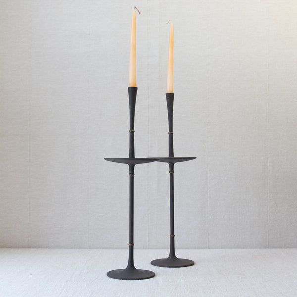 A pair of Jens Quistgaard candlesticks with off-white natural coloured candles. The black metal candlesticks are nicely contrasted by the neutral background.