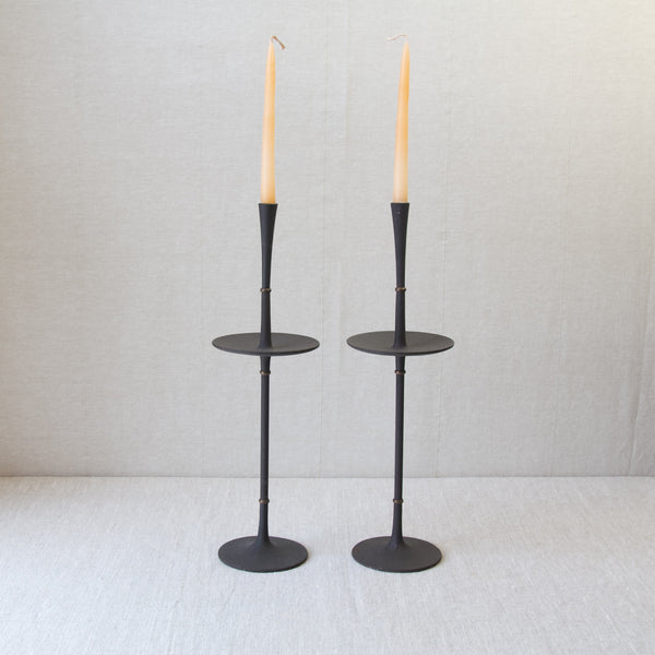 Top down view of a pair of tall slender black metal candlesticks with candles in them. This flowing, organic design is by mid-twentieth century Danish designer Jens Quistgaard.