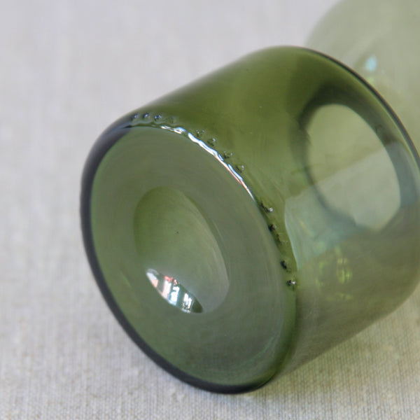 A close-up of a green glass bottle showing ripples in the glass. Kaj Franck Kremlin Kellot decanter from 1957, a sought-after example of post-war Finnish glass design.