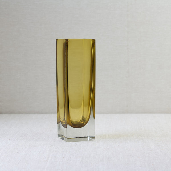 An imahg of a model 296 vase by Kaj Franck for Nuutajärvi Notsjö stood on a plain neutral coloured linen tablecloth. The bright honey-yellow coloured sommerso vase is a practical and beautiful piece of MidCentury Modern Scandinavia design.
