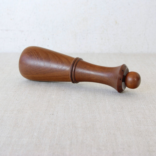 Wooden pepper grinder laying down on a beige surface with a white background. Collectible vintage Dansk Designs pepper mill 879 Jens Quistgaard mid-century modernist design