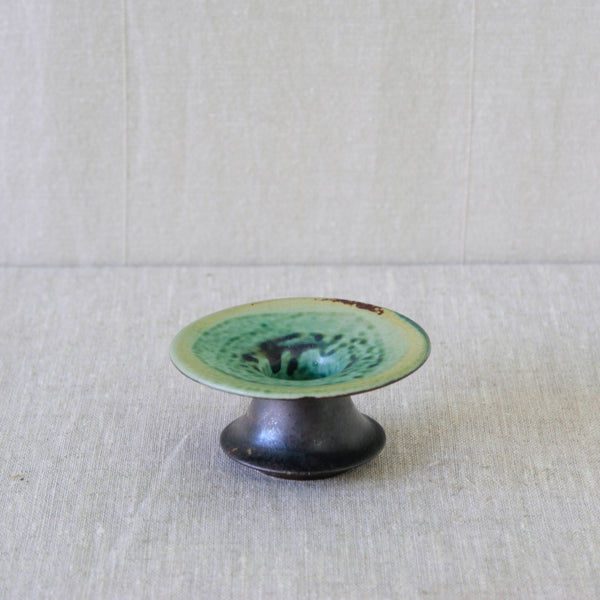 Experimental glazed ceramic candleholder by Liisa Hallamaa, with green and yellow glazes forming drips, mottling and small bubbles.
