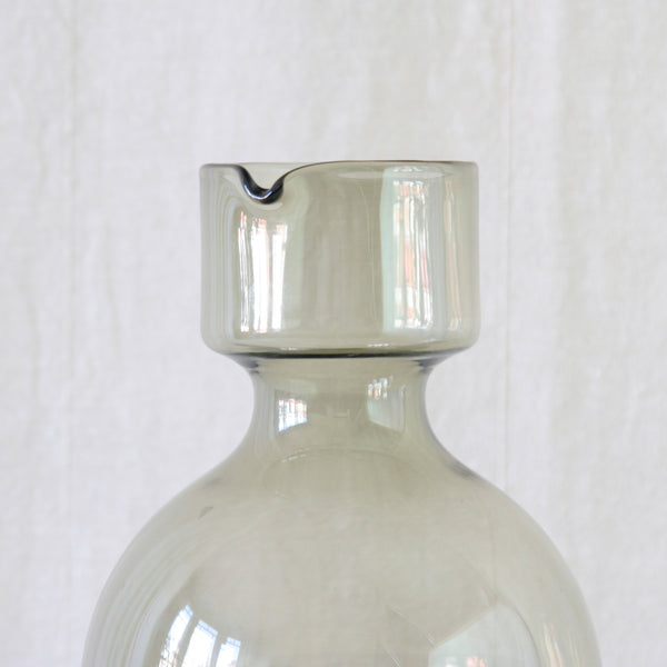 Close up of mouth and pouring lip of a smoke-grey glass pitcher forming the broad lower section of Kaj Franck's Kremlin Kellot or Kremlin Bells decanter stacking juice set.