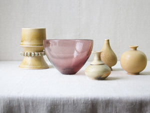 An artistic mood shot showing five highly collectible pieces of Nordic design stood atop a linen tablecloth. Included in the image is a vase by Tobo and a bowl by Gunnel Nyman