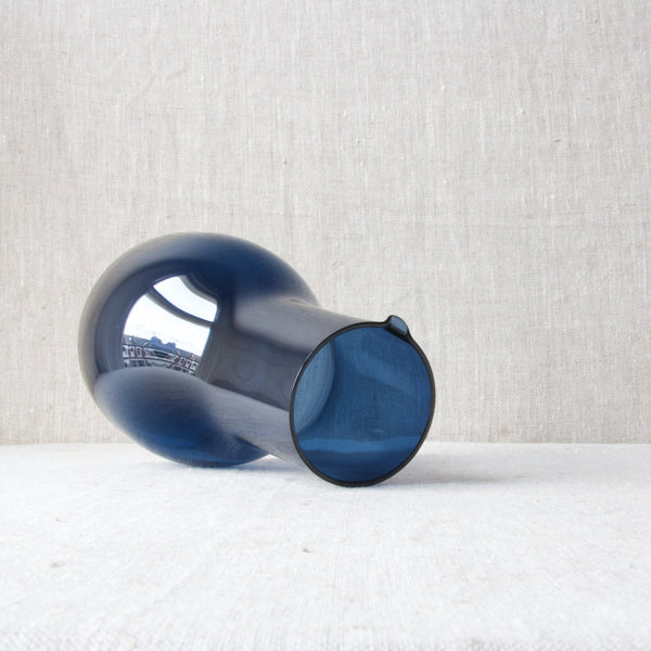 A Finnish blue glass carafe or pitcher laying on its side. This modernist design was created by Kaj Franck for Nuutajärvi Notsjö in the nineteen sixties.