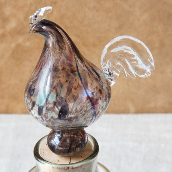 Zoomed in image of a speckled glass bird. The rooster or cockerel forms the stopper of a Head on shot of a "Kukkopullo" or “Rooster bottle” designed by Kaj Franck for Nuutajärvi Notsjö, Finland.
