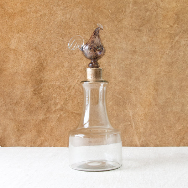 A Kukkopullo or Rooster bottle by Kaj Franck, the KF502 KF1502 model decanter stands a top a white linen sheet and against a suede textured backdrop.