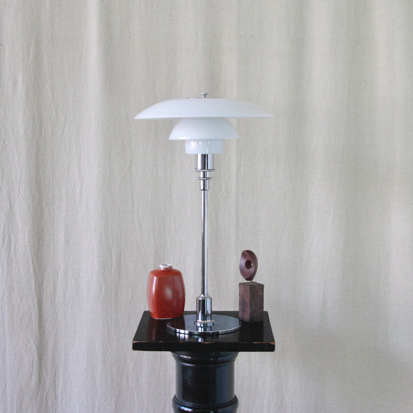 Stylish mood image showing a vintage polished chrome PH 3/2 Danish Modern light by Poul Henningsen with a red vase and Modernist sculpture.