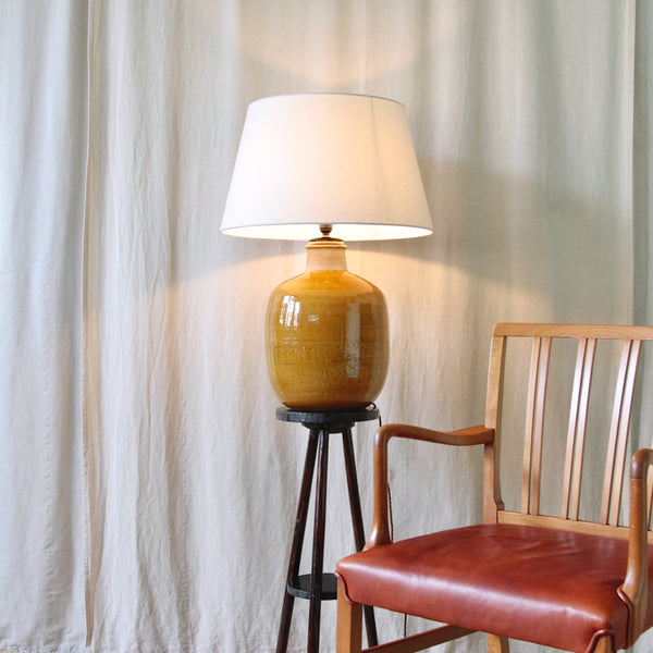 Stylish mood image of an interior featuring a Ole Wanscher chair and 1960s Danish Modern table lamp by Nils Kähler, made in stoneware at the HAK Kähler workshop in a rich ochre-yellow glaze.