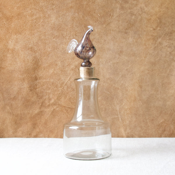 A clear and purple "Kukkopullo" or “Rooster bottle” by Kaj Franck for Nuutajärvi Notsjö. This idiosyncratic bird topped bottle is one of Kaj Franck's most recognised designs. The item is highly sought after by collectors.