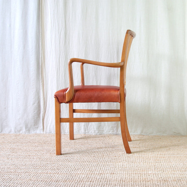 Side view of a restored Ole Wanscher Model 1675 carver chair with a warm honey-coloured beech frame and contrasting deep red leather upholstery.