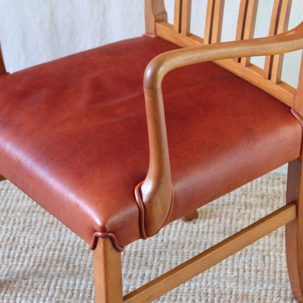 Close-up of a blonde wood Ole Wanscher 1675 armchair showing the relationship between its curved arms, spindle back and red leather seat.