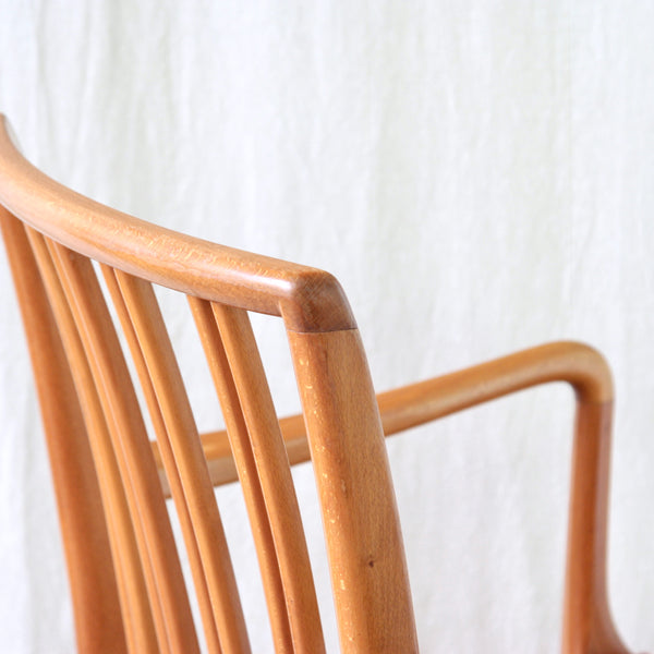 Close-up of a mid-century modern wooden armchair with a warm honey-toned finish, featuring a curved backrest and armrest. 1942 Model 1675 armchair by Ole Wanscher for Fritz Hansen, an early Danish Modern design in beech and red leather.