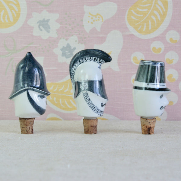 Three decorative ceramic officer figurines with stylized faces and wearing black and white helmets. Each of the Parkinson Pottery porcelain bottle stoppers retain their original cork bungs.

