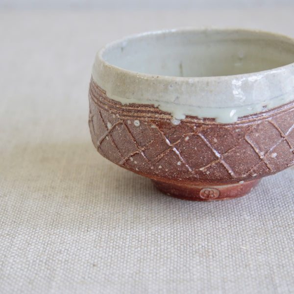 Phil Rogers stoneware chawan featuring expressive impressed lattice decoration and warm burnt-orange / brick red tonal surface.